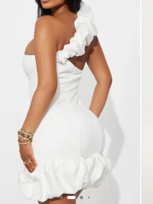 Vit oneshoulder kortklänning med volang - Säljer en vit kortklänning med oneshoulder och stora volangdetaljer vid axeln och nederkanten. Klänningen har en figurnära passform och är perfekt för dig som vill sticka ut. Materialet ser ut att vara polyester och modellen är riktigt trendig.
