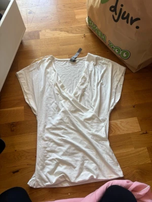 Vit omlottopp från The Black Label - Säljer en vit omlottopp från The Black Label Collection i storlek S. Toppen har korta, vida ärmar och en snygg v-ringning med omlottdesign. Tillverkad i mjuk bomull som känns skön mot huden. Perfekt till jeans eller kjol för en clean look.