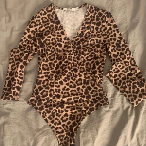 Leopardmönstrad string body NA-KD - String Body från Na-kd. Xxs men funkar xs. Är ganska djup v-ringning, åtsittande passform. Materialet är stretchigt och mjukt. Då de vart ett favvoplagg finns lite noppror kolla sista bilden.