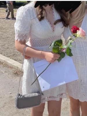 Studentklänning❤️ - Kort vit klänning i spets med v-ringning och markerad midja. Klänningen har korta ärmar med spetsdetaljer och ett genombrutet spetsband i midjan. Kjolen är lätt utställd och har fina broderade detaljer. Perfekt för student eller sommarfest.