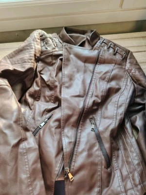 Brun skinnjacka med dragkedjor☀️ fauxläder👋🏻  - Snygg brun skinnjacka med coola detaljer som snörning på axlarna och två snedställda dragkedjor framtill🤩 Jackan har ståkrage och markerade sömmar för en modern look. Perfekt för dig som vill ha en edgy stil❤️ S-M. 