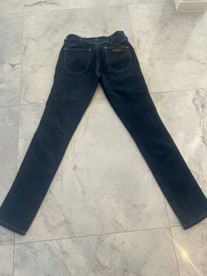 Mörkblå Levi's jeans med raka ben - Säljer ett par klassiska mörkblå jeans från Levi's med raka ben och femficksmodell. Jeansen har tydliga kontrastsömmar, Levi's ikoniska röda etikett på bakfickan och patch i läder bak i midjan. Perfekta för dig som gillar tidlös denimstil.