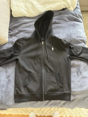 Svart set från Polo Ralph Lauren - Snyggt svart set från Polo Ralph Lauren med hoodie och matchande byxor. Hoodien har dragkedja, fickor och vit logga på bröstet. Byxorna har dragsko i midjan och vit logga på höften. Mjukt och bekvämt material, perfekt för chill dagar. Priset kan diskuteras!