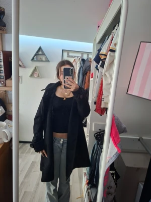 Svart lång kappa - Säljer en jätte fin svart lång kappa med klassisk krage. Rocken har en rak passform och knappar framtill. Perfekt för att ge en stilren och cool look. Passar bra till både jeans och klänning. Saknar tyvär en knapp men borde inte va så svårt att köpa en ny ock sy på. Säljer eftersom har för många jackor/kappor. Använd några gånger.