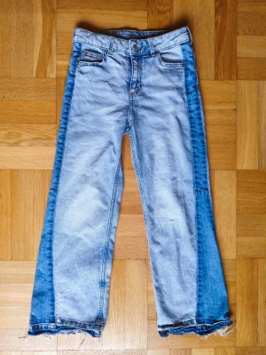 Ljusblå jeans med mörkblå paneler - Snygga ljusblå jeans med raka ben och mörkblå paneler längs sidorna. Jeansen har fyra fickor, hög midja och råa, fransiga benslut för en trendig look. Tillverkade i klassisk denim med cool tvättad effekt. Aldrig använda. Nypris 349:- 