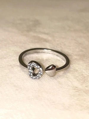Silverring med hjärtan och stenar - Trendig silverfärgad ring med öppen design, prydd med två hjärtan – ett slätt och ett dekorerat med gnistrande stenar. Stämplad 925 sterling silver 🤍🤍Billigare vid snabb affär - skicka ett prisförslag! 