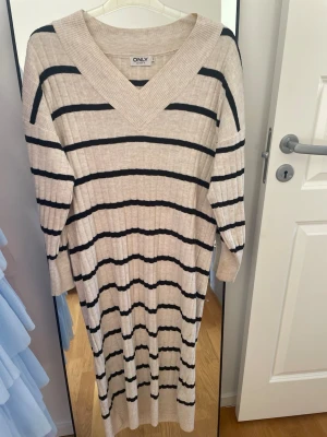 Randig ribbad klänning från ONLY - Beige långklänning från ONLY med svarta ränder. Klänningen är ribbstickad, har lång ärm och v-ringad hals. Väldigt bekväm🤗