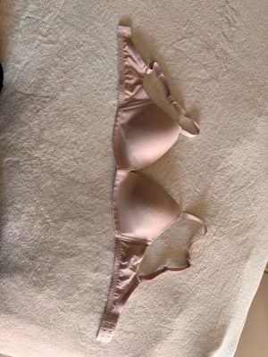 Ljusrosa vadderad bh med tunna band - Säljer en ljusrosa bh med släta, vadderade kupor och justerbara axelband. Bh:n har en enkel och stilren design utan spets eller mönster, och är tillverkad i ett mjukt, glansigt material som känns bekvämt mot huden. Endast provad.