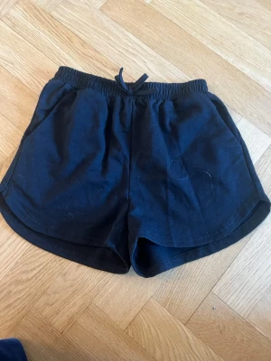 Svarta mjuka shorts med dragsko - Säljer ett par svarta shorts med elastisk midja och dragsko. Shortsen har två sidofickor och är gjorda i ett mjukt, bekvämt bomullstyg. Perfekta för chill dagar eller träning. Klassisk och enkel design.