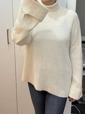 Krämvit polotröja i grovstickat - Säljer en krämvit, grovstickad polotröja med oversized passform och långa ärmar. Tröjan har ribbstickad struktur och hög polokrage, perfekt för kyliga dagar. Enkel och stilren design som är lätt att matcha med jeans eller kjol.