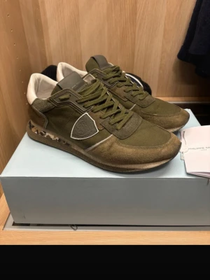 Philippe Model sneakers - Snygga olivgröna Philippe Model TRPX sneakers. Skorna har en mix av mocka och textil, samt vita partier vid hälen. Klassisk låg modell med snörning och bekväm sula. En liten defekt som man kan se i sista bilden. Syns inte när skorna är på