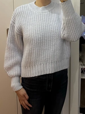 Ljusgrå chunky stickad tröja - Säljer en ljusgrå chunky stickad tröja med breda ärmar och ribbade muddar. Tröjan har en avslappnad passform och rund halsringning. Perfekt för att hålla sig varm och snygg under kyliga dagar.