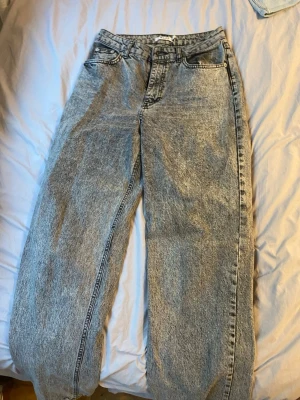 Acid wash jeans från NA-KD - Säljer ett par snygga acid wash jeans från NA-KD med hög midja och raka, vida ben. Jeansen har klassisk femficksdesign och bälteshällor. Perfekta för dig som gillar en retro och avslappnad stil.