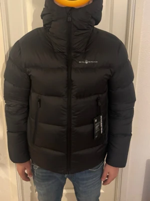 Sail Racing Jacka - helt ny - Snygg svart pufferjacka från Sail Racing cloud down hood heter modellen helt splitter ny. Nypris - 4500kr.                                                      Mitt pris - 1500kr.                                                      pris kan diskuteras ifall man är seriös                 Först till kvarn!!! För den har ett litet hål i jackan 