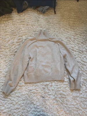 Beige polotröja i mjuk stickad kvalitet - Säljer en beige stickad polotröja med ribbade muddar och hög krage. 