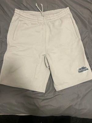 Beige shorts från Limitless Humanz - Snygga beige shorts från Limitless Humanz med elastisk midja och snörning. Shortsen har två sidofickor och en diskret logga i blått på ena benet. Perfekta för varma dagar och chill stunder.