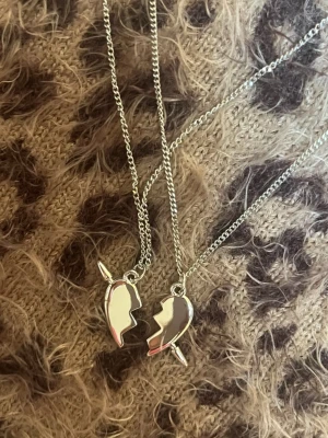 Silverfärgade bästa vän-halsband - Två matchande halsband i silverfärg med berlocker formade som två halvor av ett hjärta som passar ihop. Perfekt för att dela med en vän. Kedjorna är tunna och blanka, och berlockerna har en enkel, stilren design. Rostfri 