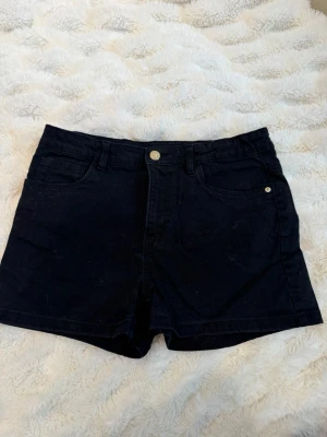 Svarta denimshorts med fickor - Snygga svarta shorts i denim med klassisk femficksdesign och knappstängning framtill. Perfekta för en avslappnad stil och passar till det mesta. Shortsen har bälteshällor och raka ben.
