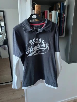 Royal Academy långärmad t-shirt - Snygg långärmad t-shirt från Royal Academy i mörkgrått med vita ärmar och tryck framtill. Klassisk krage och kontrastdetaljer vid halsen. Perfekt för en avslappnad och trendig stil. Tillverkad i mjuk bomull för skön känsla.