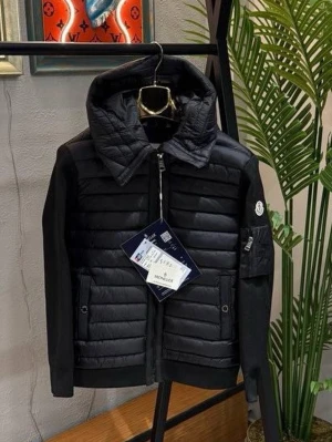 Svart pufferjacka från Moncler - Stilren svart pufferjacka från Moncler med quiltad front och huva. Jackan har stickade ärmar, dragkedja framtill och en ficka med Moncler-logga på ärmen. Perfekt för kalla dagar och ger en modern look.