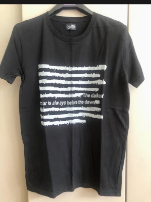 Svart t-shirt med tryck och text - Cool svart t-shirt från Sixth June med vitt tryck och texten 'The darkest hour is always before the dawn' på framsidan. Klassisk rund hals och korta ärmar. Perfekt för en avslappnad streetstyle-look.