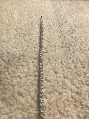 Glittrigt silverfärgat tennisarmband - Ett stilrent tennisarmband i silverfärg med gnistrande stenar längs hela bandet. Armbandet har en klassisk, smal design som ger en elegant look. Perfekt för dig som gillar att addera lite extra bling till din outfit.