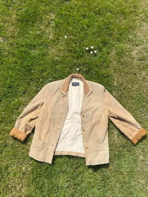 Beige mockajacka från Collin - Våreeens kap en beige mockajacka från Collin med klassisk krage och knäppning framtill. Jackan har uppvikta ärmslut i en något mörkare ton och två fickor framtill. Den e använd men lite sliten på ett snyggt sätt 