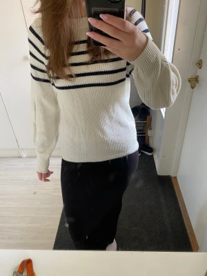Vit stickad tröja med marinblå ränder - Vit stickad tröja från Kappahl med marinblå horisontella ränder över bröstet och axlarna. Tröjan har rund halsringning, långa ärmar och ribbstickade muddar. Perfekt för en avslappnad och stilren look.