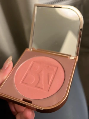 BeautyAct puderrouge i persikorosa - Säljer ett puderrouge från BeautyAct by KICKS i en snygg persikorosa nyans. Rouget kommer i en fyrkantig, guldig dosa med spegel i locket och har BeautyAct-loggan präglad i pudret. Perfekt för att ge kinderna en fräsch glow.