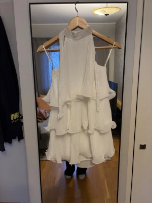 Vit omlottklänning med volanger - Säljer en superfin vit kortklänning med omlottkrage. Klänningen har flera lager volanger och är gjord i ett lätt, plisserat tyg som ger en luftig känsla. Perfekt till midsommar eller skolavslutning. Aldrig använd med prislapp kvar, nypris 459kr. Storleken är one size men skulle säga s/xs.