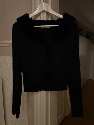 Svart cardigan med päls-krage - Svart cardigan med lång ärm och en mjuk päls krage. Tröjan har en knapp framtill och är i ett tunt, stretchigt material. Använd 1 gång, så i ett väldigt bra skick💕 