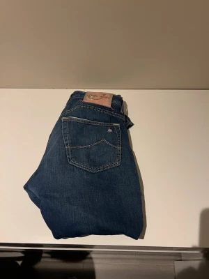 Blåa jeans från Jacob Cohen - Snygga blå jeans från Jacob Cohen med klassisk femficksdesign och kontrastsömmar. Jeansen har en patch med logga bak i midjan och en liten broderad stjärna på ena bakfickan. Perfekta för en avslappnad och trendig look.