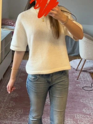 Vit stickad topp med kort ärm - Mysig vit stickad topp med korta ärmar och rund hals. Enkel och stilren design som passar perfekt till jeans eller kjol. Ribbad kant vid ärmslut och nederkant för en snygg finish.