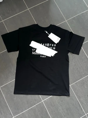Svart Maison Margiela t-shirt - Säljer en svart t-shirt från Maison Margiela. Storlek M. Det är en perfekt tröja inför sommaren. Tags och e-kvitto följs med. Endast 600kr.