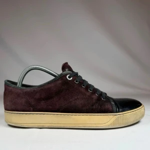 Vinröda Lanvin - Snygga sneakers i vinröd Lanvin mocka med svart, glansig tå och svarta skosnören. Skorna har en beige sula och klassisk låg profil. Perfekta för dig som vill ha en stilren men unik look.