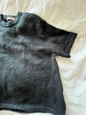 Mörkblå stickad t-shirt - En oversized mörkgrå stickad t-shirt med korta ärmar och rund hals. Tröjan har en avslappnad passform och ribbade kanter vid hals, ärmslut och nederkant. Perfekt för lager på lager och en chill look.