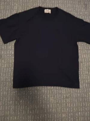 Mörkblå ami Paris  t-shirt - Stilren och tidlös tröja från Ami Paris i 100% bomull. Tröjan har en avslappnad passform med korta ärmar och en minimalistisk design som gör den enkel att matcha med både jeans och mer uppklädda outfits. Den mörka färgen ger ett elegant och sofistikerat uttryck, perfekt för både vardag och finare tillfällen.  Tillverkad i mjuk och högkvalitativ bomull som ger en skön känsla hela dagen. En riktig garderobsklassiker för dig som uppskattar stilren design och bra kvalitet.