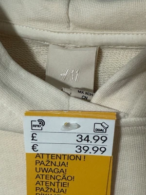 Beige hoodie från H&M - Stilren beige hoodie från H&M med avslappnad passform och ribbade muddar vid ärmslut och nederkant. Tillverkad i mjuk bomullsblandning och har en klassisk huva utan snören. Perfekt för en enkel och clean look.