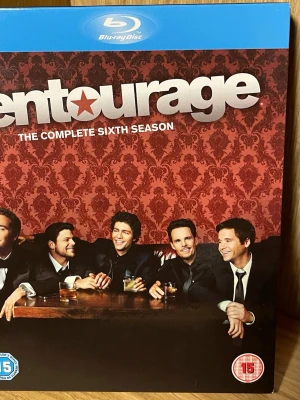 Entourage Säsong 6 Blu-ray - Blu-ray box med hela sjätte säsongen av tv-serien Entourage. Omslaget har röd bakgrund med mönster och visar huvudkaraktärerna vid ett bord. Innehåller bonusmaterial och gästframträdanden. Text och ljud på flera språk.