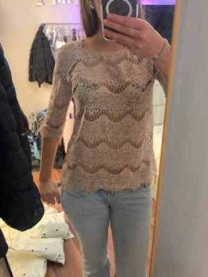 Beige spetsblus med trekvartsärm - Säljer en beige blus i spets med vågigt mönster och trekvartsärm. Blusen har rund halsringning och är lätt transparent, perfekt för att styla med ett linne under. Superfin detalj med den vågiga kanten nertill.