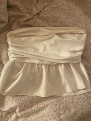 Vit tubtopp - Snygg vit axelbandslös tubtopp med peplumvolang och draperad överdel. Perfekt att styla med jeans eller kjol för en trendig look. Mjuk och bekväm känsla.