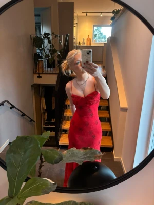 Adoore klänning - Snygg röd långklänning med tunna axelband och blommigt mönster av rosor. Klänningen har en figurnära passform och lätt utsvängd nederdel. Perfekt för sommarens alla tillfällen.