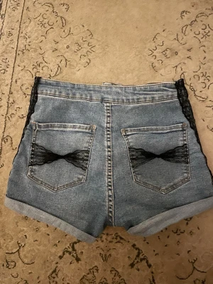 Jeansshorts med spets rosett bak och på sidan  - Säljer dessa fina jeans shorts med spetsrosetter på bakfickorna och på sidan. Är originellt från H&M tror jag, men hittar ingen lapp.  De är ganska stretchiga, rätt säker på att de är en XS Spetsen sydde jag på själv Tycker de formar en väldigt fint speciellt bakifrån.  Tyvärr för små för mig, kan inte knäppa dem där fram men senaste tiden brukade jag vika ner dem som jag gjort på bilderna. Gaven mer lågmidjad look men de är egentligen högmidjade. Har fler bilder. 