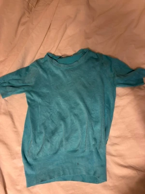Turkos kortärmad topp - En enkel turkos topp med korta ärmar och rund hals. Toppen har ribbade kanter nedtill och vid ärmsluten, vilket ger en snygg passform. Perfekt att matcha med jeans eller kjol för en avslappnad look.