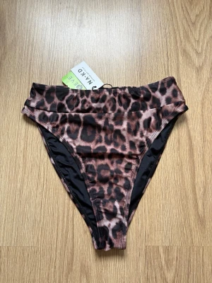 Leopardmönstrad bikiniunderdel NA-KD - Snygg bikiniunderdel från NA-KD med leopardmönster i bruna och svarta toner. Modellen är high waist och har en klassisk passform som ger en trendig look på stranden. Tillverkad i mjukt och stretchigt material för bästa komfort ☀️