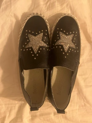 Svarta loafers med stjärndetaljer - Säljer ett par svarta loafers med silvriga nitar och glittrande stjärnor på ovandelen. Använda max 2 ggr.