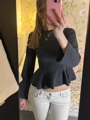 Mörkgrå peplum topp med utsvängda ärmar - Snygg mörkgrå topp med peplum och utsvängda långärmar. Toppen har en figurnära passform upptill och markerad midja som ger en feminin siluett. Perfekt att styla med jeans eller kjol för en trendig look. Tröjan har inte kommit till användning då jag har den i flera färger.