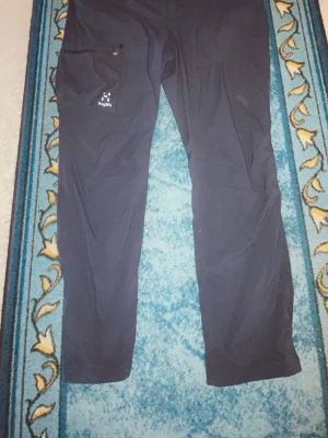 Svarta byxor från Haglöfs sällsynta  - Säljer ett par svarta byxor från Haglöfs med rak passform och dragkedjeförsedd ficka på sidan. Byxorna är tillverkade i ett lätt och slitstarkt material, perfekta för dig som gillar outdoor och friluftsliv. Diskret logga på vänster ben.