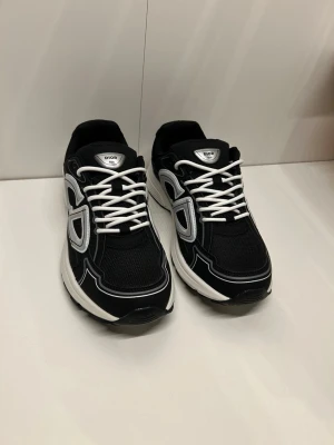Svarta b30 sneakers  - Snygga svarta b30 sneakers med vit och silverfärgad logga på sidan, vita snören och tjock vit sula. Ovandelen är i mesh och mockaliknande material för en sportig vibe. Perfekta för dig som vill ha en exklusiv och trendig look.
