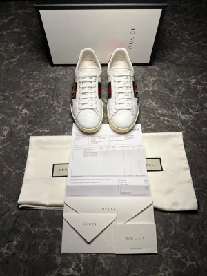 Gucci ace + kvitto - Säljer ett par otroligt snygga skor från det exklusiva märket Gucci! Skorna är i mycket bra skick, skulle säga ungefär 8,7/10. Vid köp tillkommer även allt OG, alltså skorna, skolådan, dustbags, kvitto och kort. Nypris ligger på över 9000kronor men vi säljer våra för endast 2299 och kan gå ner i pris ännu mer vid snabb affär! Skorna är i storlek 42 och är true to size (28cm). Skriv gärna ifall det är några funderingar, allt bästa SkoKapet